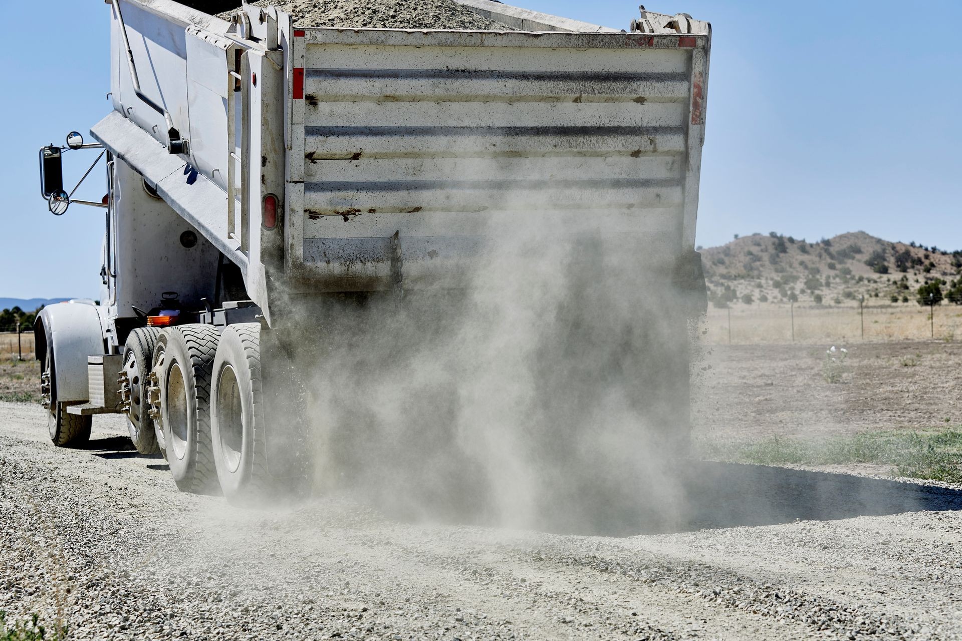 A dump truck spreading gravel on a dirt driveway
