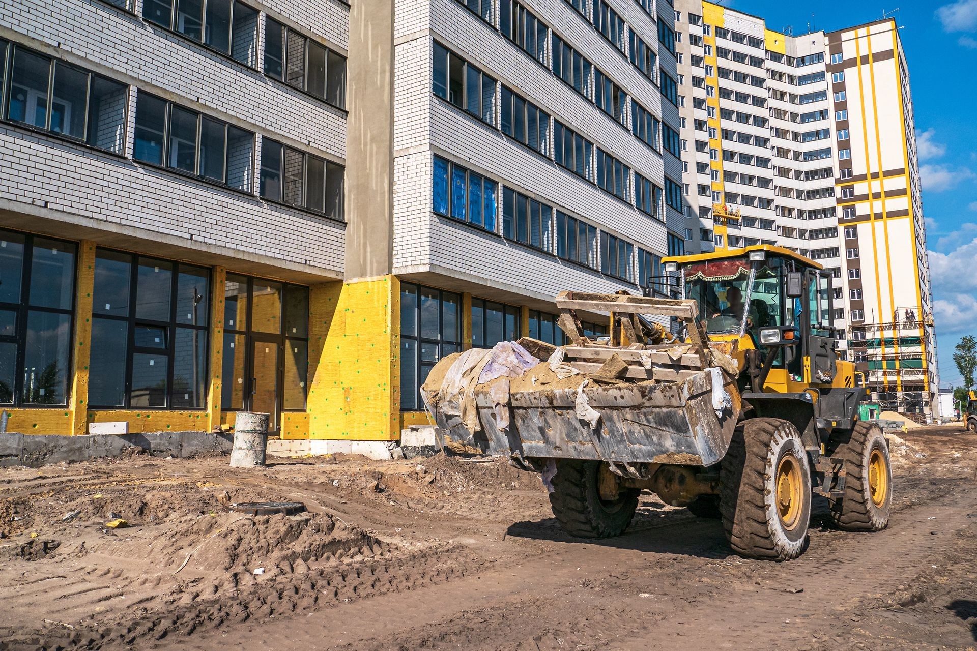 Bulldozer excavator carrying construction debris in bucket on construction site with new building on background, industrial machinery at work.